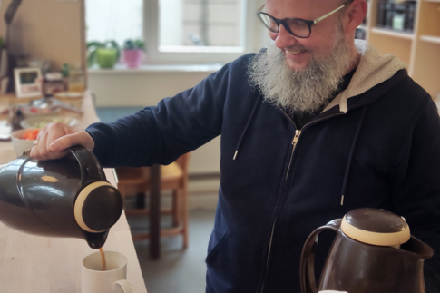 Ein ehrenamtlicher Mann schenkt einem Besucher, der nicht im Bild zu sehen ist, einen frischen Kaffee ein.