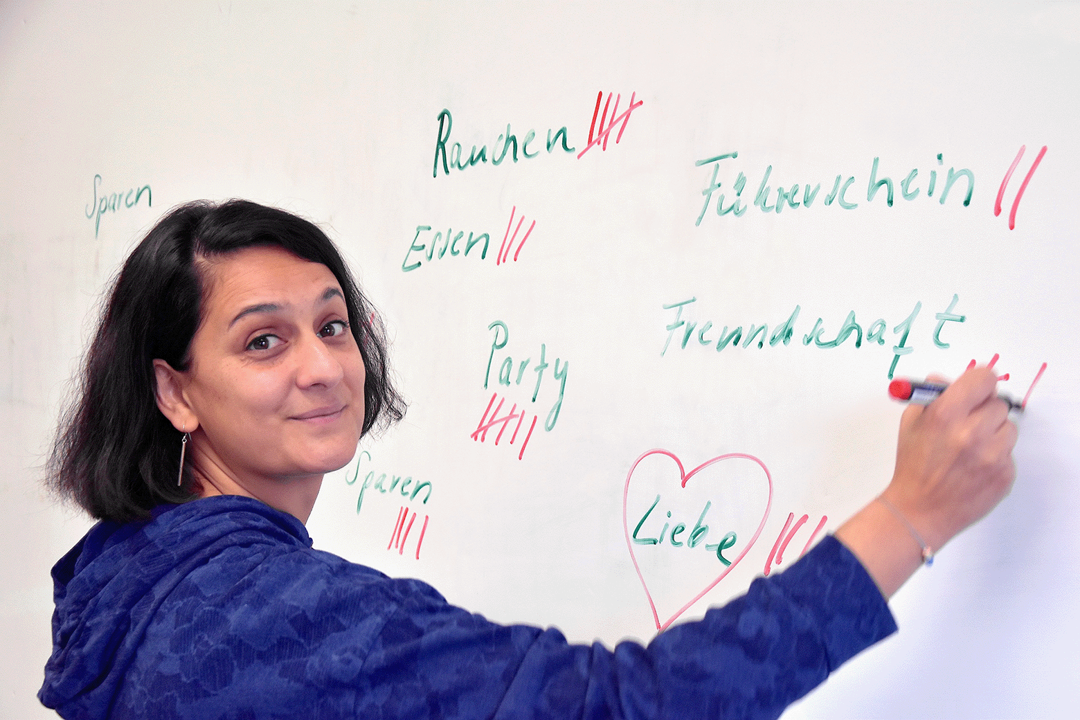 Navina De steht vor einem Whiteboard und schreibt Begriffe auf, die finanzielle Asugaben betreffen.